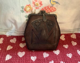 May include: A brown leather coin purse with a decorative floral design and a silver clasp.