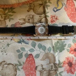 May include: A silver-toned wristwatch with a black leather band. The watch face has a white background with black markings and a silver-toned logo. The watch is 5 inches long.