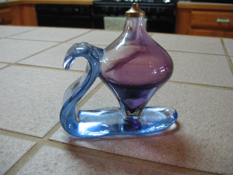 May include: A purple glass bottle with a blue glass base. The bottle is shaped like a teardrop and has a small opening at the top. The base is shaped like a swan.