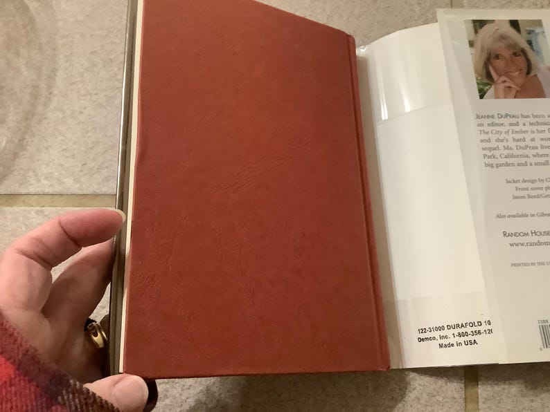 Puede incluir: Un libro abierto con una cubierta roja y p&aacute;ginas blancas. El lomo tiene un borde dorado. El libro se sostiene abierto, revelando texto y una foto de una mujer en la p&aacute;gina derecha. El texto "Made in USA" es visible.