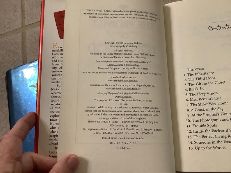 Puede incluir: Libro abierto con texto en las p&aacute;ginas. La p&aacute;gina izquierda tiene un resumen del libro, y la p&aacute;gina derecha tiene una tabla de contenido. El libro se titula "The Prophet of Yonwood" de Jeanne DuPrau.