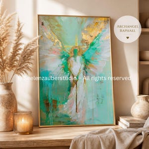 May include: Abstract painting of an angel with turquoise, gold, and white brushstrokes, framed in a gold-coloured frame. The artwork features the text "ARCHANGEL RAPHAEL" in a white circle. The image is displayed on a wooden surface.