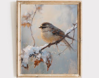 以下が含まれることがあります： 金色の額縁に入った油絵で、雪に覆われた細い枝にとまる茶色とベージュの小さな鳥が描かれています。背景は柔らかく落ち着いた青とベージュの色調で、目に見える筆致と「LUX DESIGN Collection」という文字が記されています。