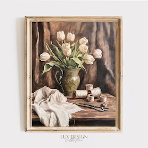 May include: A framed still life painting featuring a bouquet of white tulips in a green vase. Spools of thread, scissors, and a white cloth are on a wooden table. The background is a dark brown fabric.