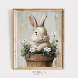 Puede incluir: Pintura enmarcada de un conejo marrón claro con orejas largas, metido en una maceta marrón llena de margaritas blancas y hojas verdes. La pintura tiene un fondo suave y neutro y un marco dorado. El texto "LUX DESIGN Collection" está en la parte inferior.