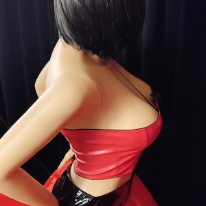 Könnte beinhalten: Eine Schaufensterpuppe in einem rot-schwarzen Outfit. Das Oberteil ist glänzend rot mit schwarzem Besatz und dünnen Trägern. Der Rock ist aus rotem Tüll. Die Schaufensterpuppe hat kurze schwarze Haare.