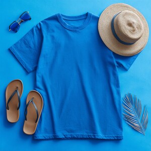 May include: A blue crew neck t-shirt with a straw hat, sunglasses, and flip-flops arranged on a blue background. The hat has a blue band. The sunglasses have blue lenses and gold frames. The flip-flops are brown and black.