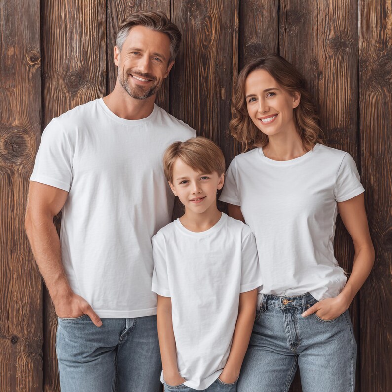 May include: A family of three wearing matching white t-shirts and blue jeans, posing in front of a wooden wall. The family includes a man, a woman, and a child, all smiling at the camera. The t-shirts are plain and the jeans are a light wash.