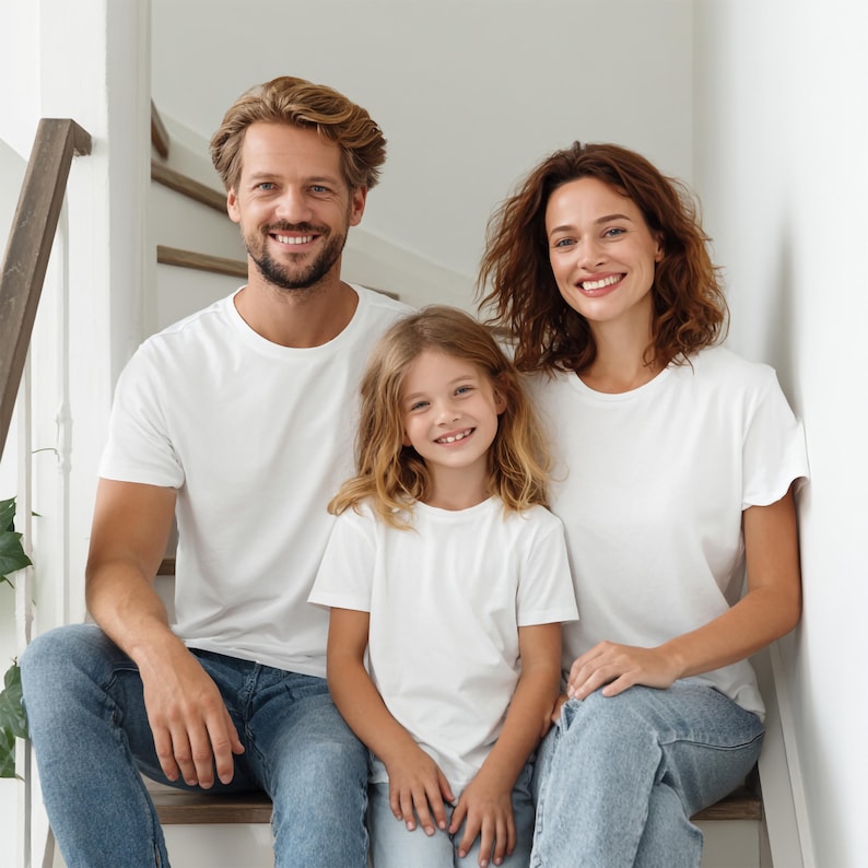 May include: A family of three, smiling and posing on a staircase. They are wearing matching white t-shirts and blue jeans. The background includes a white wall and wooden staircase.