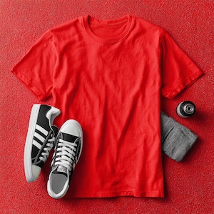 May include: A red crew neck t-shirt, black and white sneakers, a gray wristband, and a black camera lens are arranged on a red textured surface. The sneakers have white soles and laces. The wristband is folded.