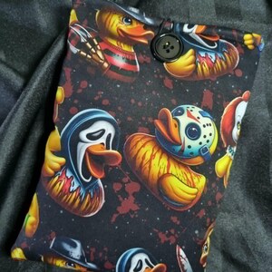 May include: A rectangular fabric pouch featuring a black background with a repeating pattern of yellow rubber ducks dressed as horror movie characters, including hockey masks and ghost masks, secured with a single black button closure.