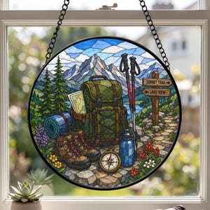 Op de afbeelding: Een ronde glas-in-lood zanger met een wandelscène, inclusief een groene rugzak, bruine wandelschoenen, een blauwe waterfles, een kompas en wandelstokken. Een houten wegwijzer toont de teksten SUMMIT TRAIL en LAKE VIEW bij een berglandschap.