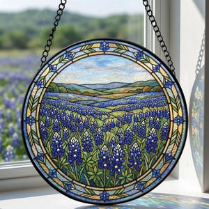 May include: Round stained glass window art depicting a field of bluebonnets under a blue sky. The artwork is framed with a black metal chain for hanging. The window art features a detailed floral design with shades of blue, green, and yellow.
