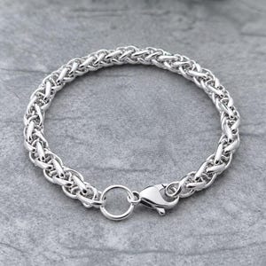 May include: A silver-toned chain bracelet featuring a complex, woven wheat-style link pattern. The bracelet is secured with a polished lobster claw clasp and a circular jump ring, showcasing a consistent metallic finish throughout the entire piece.
