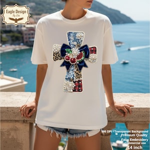 Pode incluir: Uma camiseta branca com um design de cruz, laço, cerejas e vários padrões. A cruz é adornada com pérolas e lantejoulas. A imagem também inclui o texto "Eagle Design by Ede" e uma medida de 35.56 cm.