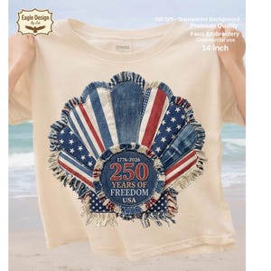 Puede incluir: Camiseta color crema con un diseño patriótico. El diseño incluye una forma de concha de mezclilla con rayas rojas y blancas, estrellas azules y un emblema circular que dice "250 Years of Freedom USA" con los años 1776-2026. El diseño mide aproximadamente 35.5 cm.