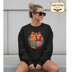 Könnte beinhalten: Schwarzes Sweatshirt mit einem farbenfrohen Basketball-Design mit einer Schleife. Der Basketball ist in vier Abschnitte mit verschiedenen Mustern und Farben unterteilt. Das Sweatshirt hat lange Ärmel und einen Rundhalsausschnitt.