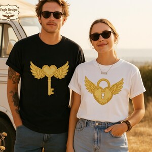 May include: Two people wearing t-shirts with gold-colored heart and wing designs. One shirt is black, featuring a key design, and the other is white, with a lock design. Both shirts have short sleeves and are paired with blue jeans.