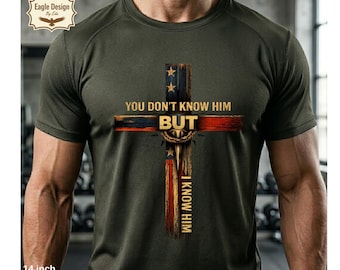 May include: Olive green t-shirt featuring a cross design with the text "YOU DON'T KNOW HIM BUT I KNOW HIM." The cross incorporates elements of the American flag. The shirt is 14 inches in length and suitable for commercial use.