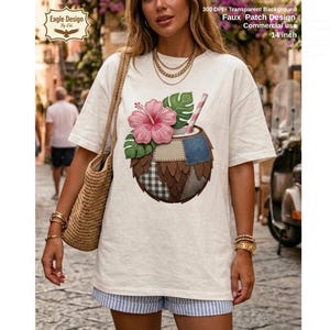 May include: A cream-coloured t-shirt with a vibrant coconut drink design. The design features a pink hibiscus flower, green leaves, and a striped straw. The shirt also has the text "Faux Patch Design Commercial use 14 inch".