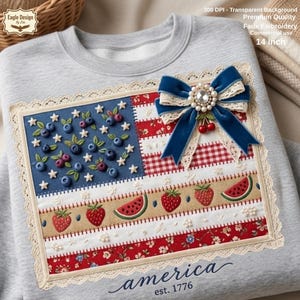 Può includere: Una felpa grigio chiaro con un design a bandiera americana ricamato. La bandiera presenta mirtilli, fragole e anguria. Un fiocco di velluto blu con un centro gioiello e ciliegie accentua il design. Il testo "america est. 1776" è scritto in basso.