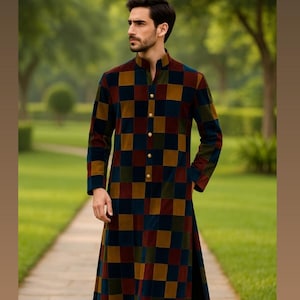 May include: A long, chequered coat in shades of burgundy, navy, and gold. The coat has a mandarin collar and gold buttons. The garment is worn outdoors on a stone path, with a blurred green background.
