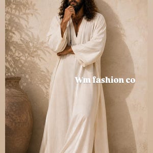 May include: A long-sleeved, floor-length off-white robe with a V-neckline and side slits. The garment features a textured fabric and the text Wm fashion co is printed in white on the right side of the robe. The robe is worn with brown sandals.