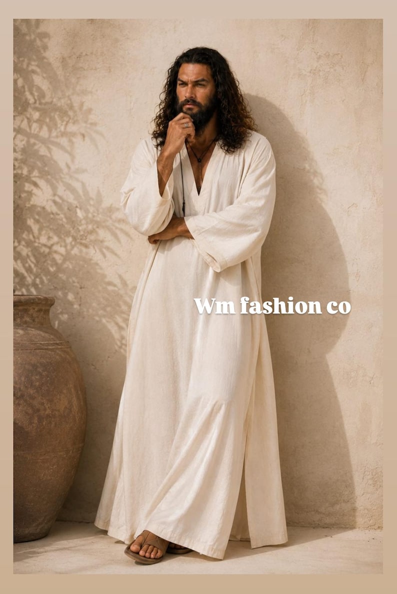 May include: A long-sleeved, floor-length off-white robe with a V-neckline and side slits. The garment features a textured fabric and the text Wm fashion co is printed in white on the right side of the robe. The robe is worn with brown sandals.