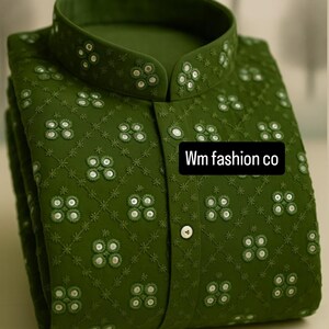 Puede incluir: Camisa bordada verde oliva con cuello mandarín y abotonadura frontal. La camisa presenta un patrón floral repetido con pequeños detalles blancos. El texto "Wm fashion co" es visible en la parte delantera.