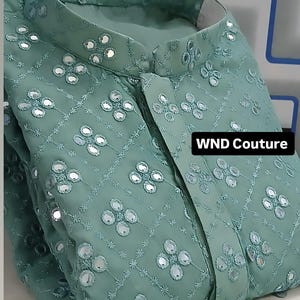 Puede incluir: Una kurta verde claro bordada con cuello mandarín. La tela está adornada con adornos de espejo en un patrón floral. El texto "WND Couture" es visible en la esquina inferior derecha.