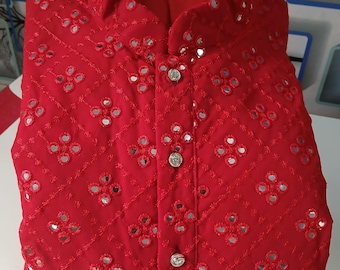 May include: A bright red, collared shirt with intricate embroidery and small, reflective mirror accents. The shirt features a button-up front and a quilted pattern throughout the fabric. The design is symmetrical, with floral-like patterns.