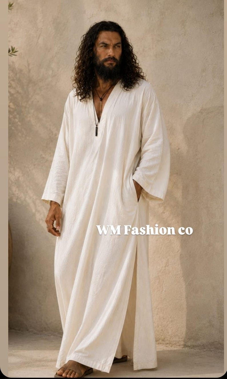May include: A long-sleeved, floor-length off-white robe featuring a V-neckline, side pockets, and high side slits. The garment displays the text WM Fashion co on the front. The fabric has a textured appearance, and the design includes a simple cut.