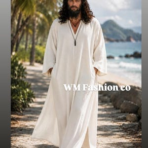 May include: A long-sleeved, floor-length off-white tunic with a V-neckline and side slits, featuring the text WM Fashion co. The garment has a loose, flowing fit with wide sleeves and is made of a lightweight, textured fabric.