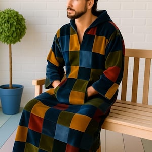 Puede incluir: Una bata con capucha con un dise&ntilde;o de patchwork en tonos azules, dorados, rojos y verdes. La bata tiene un bolsillo delantero y la lleva una persona sentada en un banco de madera. La bata est&aacute; hecha de un material suave y afelpado.