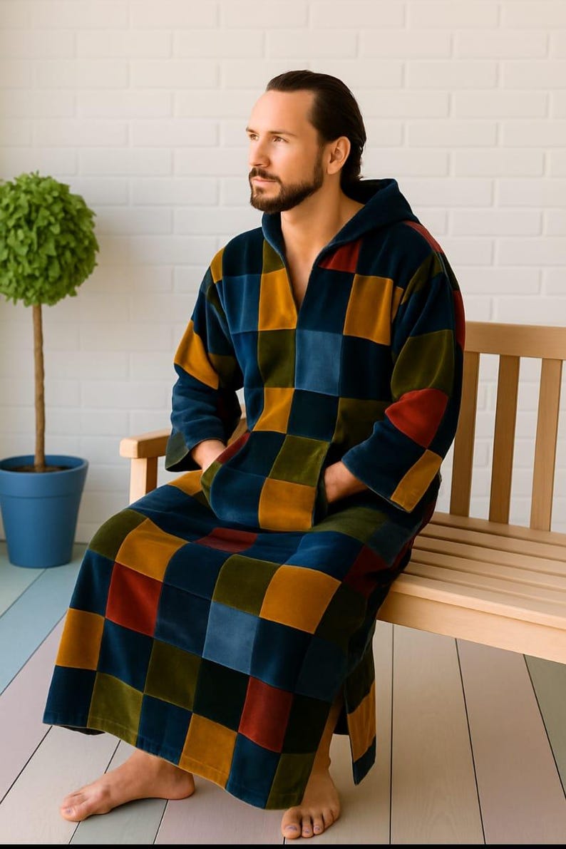 Puede incluir: Una bata con capucha con un dise&ntilde;o de patchwork en tonos azules, dorados, rojos y verdes. La bata tiene un bolsillo delantero y la lleva una persona sentada en un banco de madera. La bata est&aacute; hecha de un material suave y afelpado.