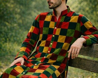 May include: A long-sleeved, button-down garment with a vibrant checkerboard pattern in red, yellow, green, and brown. The garment has a mandarin collar and is made of a soft, velvety material. The person is sitting on a wooden bench.