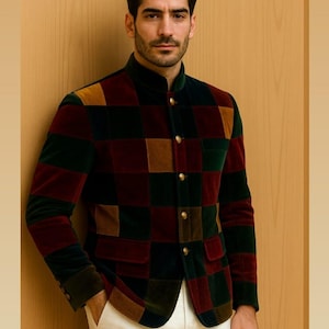 May include: A multi-colored patchwork jacket with a mandarin collar and gold buttons. The jacket features a pattern of burgundy, green, brown, and gold squares. The person is wearing white pants. The jacket is made of a velvet-like material.