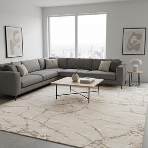 Può includere: Un moderno soggiorno con un ampio divano angolare grigio, un tavolino in legno chiaro con gambe nere e un tappeto fantasia. Due opere d'arte astratte incorniciate sono appese al muro. La stanza ha una palette di colori neutri.