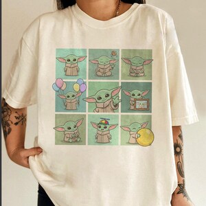 May include: Cream-coloured t-shirt featuring a grid of nine illustrations of a green alien character. Each illustration shows the character in different poses, holding items like balloons and a yellow ball. The design is set against a light green background.