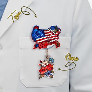 May include: A patriotic badge reel with a United States map design featuring the American flag, the text "1776-2026", and a floral charm. The badge reel is attached to a white pocket.