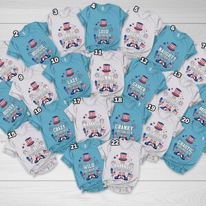 May include: A collection of baby and toddler t-shirts in various colors, each featuring a patriotic firecracker design with text. The shirts have short sleeves and are suitable for Independence Day celebrations.