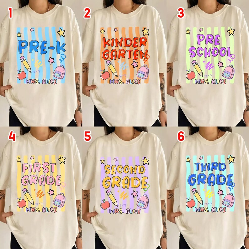 以下が含まれることがあります： 学校のグレードレベルのデザインが施されたクリーム色のTシャツ。各シャツには、鉛筆、リンゴ、バックパック、星とともに、カラフルなストライプのボックスにグレードレベルの名前が記載されています。「MRS. ALICE」の文字が下に印刷されています。