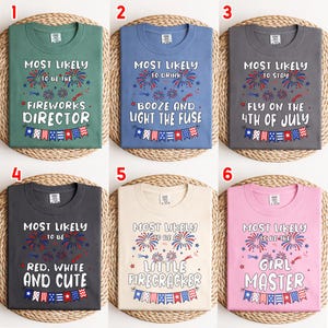 May include: Six different-colored t-shirts with text related to the 4th of July. The shirts are green, blue, gray, dark gray, beige, and pink. Each shirt has a different phrase, such as "Fireworks Director" or "Little Firecracker", with fireworks and banner graphics.