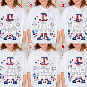 May include: White t-shirts with patriotic designs. Each shirt features a red, white, and blue top hat, fireworks, stars, and the text "The Sassy Firecracker", "The Bougie Firecracker", "The Party Firecracker", "The Loud Firecracker", "The Head Firecracker", and "The Naughty Firecracker".