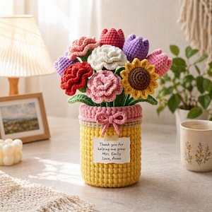 May include: A handmade crochet bouquet of colorful flowers in a yellow vase with a pink rim and bow. The bouquet includes red, pink, white, yellow, and purple flowers. A small tag reads, "Thank you for helping me grow Mrs. Emily Love, Anna."