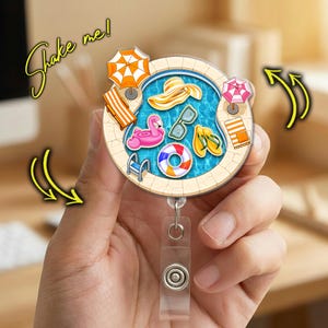 May include: A round, summer-themed badge reel featuring a pool design with a flamingo float, sunglasses, and a beach hat. The badge reel has a clear plastic strap and a metal clip. The words "Shake me!" are written in a yellow script.