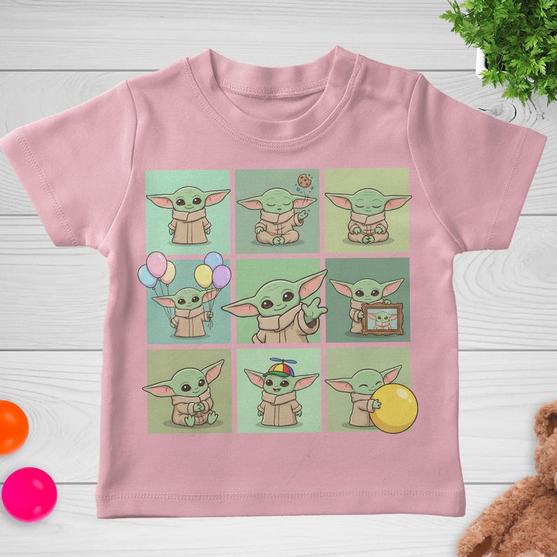 May include: Pale pink baby t-shirt with a grid of nine cartoon images of a green alien character. Each image shows the character in different poses, some holding balloons or a ball. The t-shirt is made of a soft material.