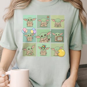 May include: Pale green t-shirt with a grid of nine illustrations of a green alien character. The character is shown in different poses, holding balloons, a cookie, and a yellow ball. The illustrations are set against a light green background.