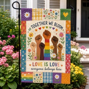 May include: A rectangular garden flag featuring a patchwork border of floral and rainbow patterns. The center displays raised fists of various skin tones, one with a rainbow sleeve, surrounded by flowers and the text Together We Bloom and Love Is Love everyone belongs here.