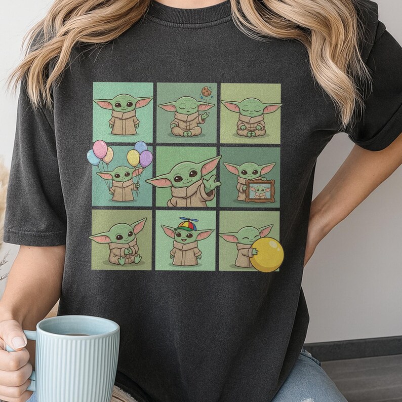 May include: Dark grey t-shirt with a grid of nine cartoon images of a green alien character in different poses. The character wears a tan robe and holds balloons, a cookie, and a yellow ball.